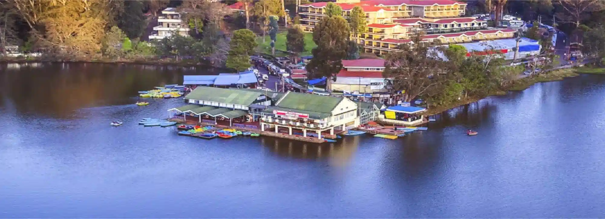 High angle view of Kodaikanal Lake showing the boat house, colorful rowboats and lakeside resorts nestled among trees.