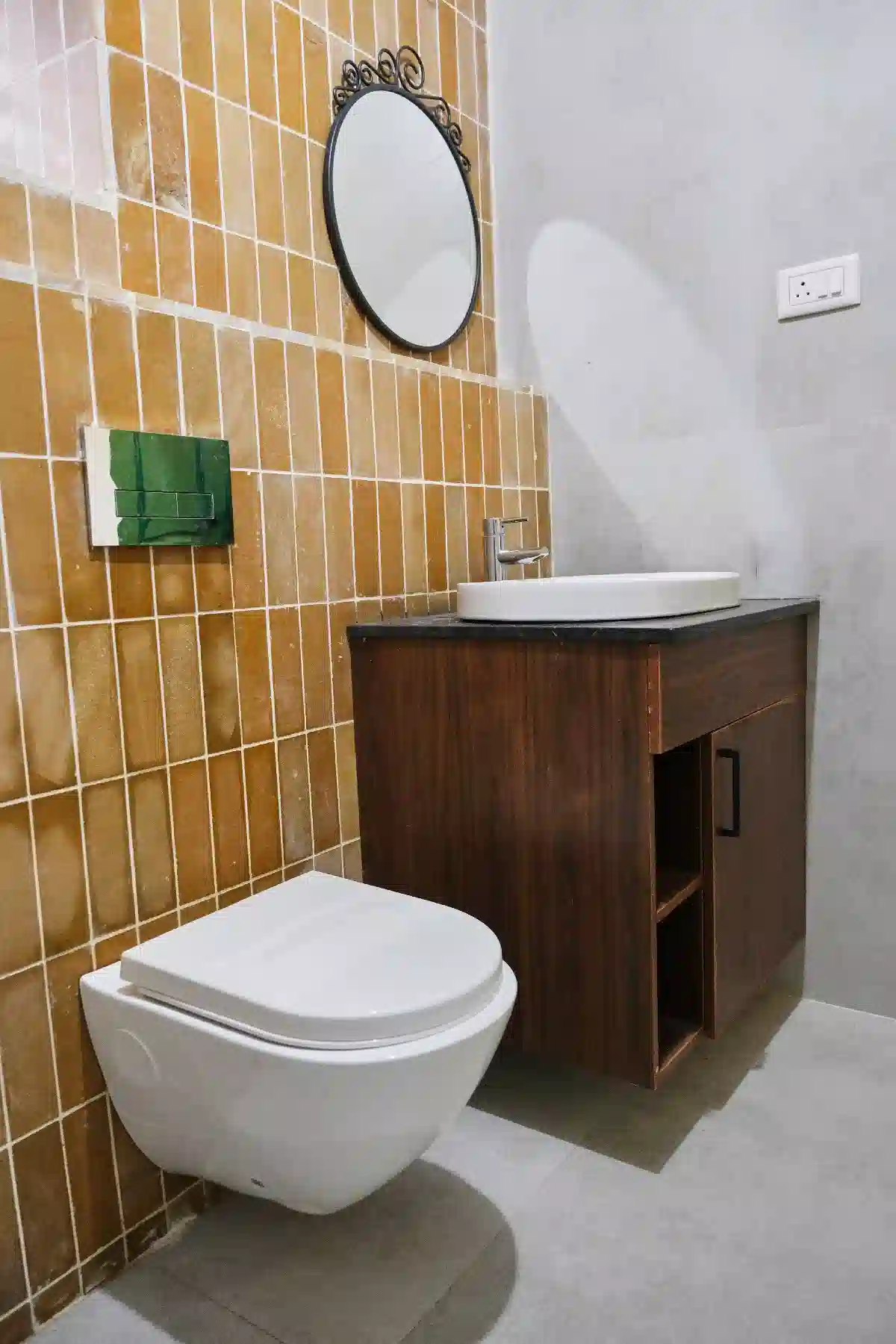 Stylish Cardamom Pods bathroom for two with vertical ochre tiles, round mirror and a wall-mounted toilet for modern comfort.