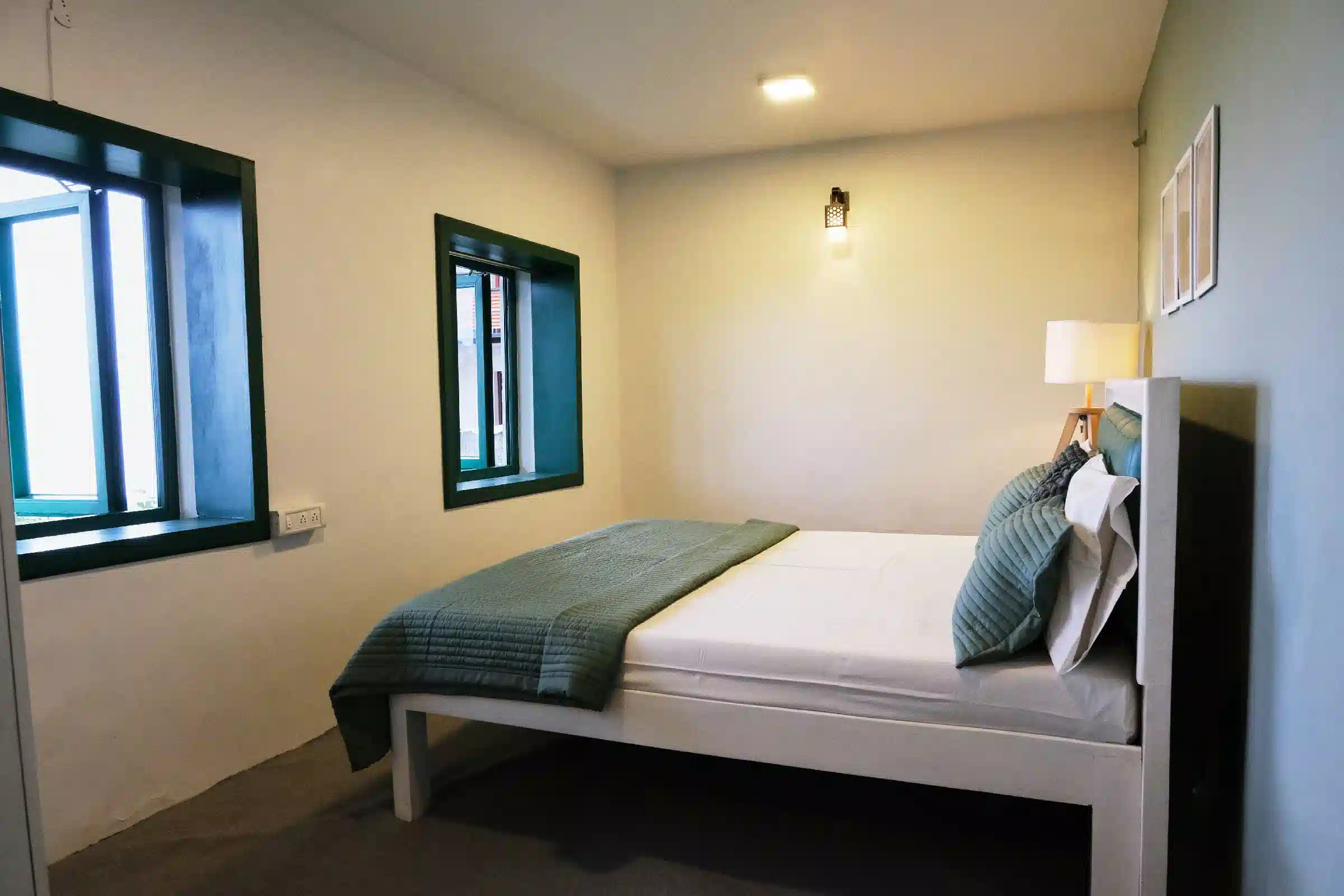 Bright couple's bedroom at Cardamom Pods featuring a queen bed, green window frames and soft minimalist interior decor.